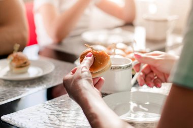 Mutlu bir aile masada kahvaltı yapıyor. Mini burgerler masada ve kadınların elinde.