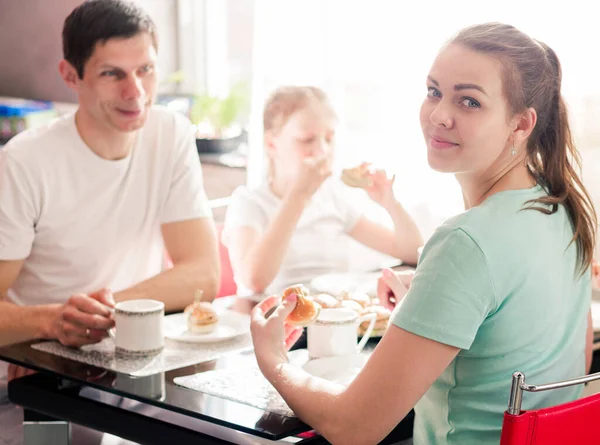 Een gelukkig gezin ontbijt aan een tafel in de keuken in hun appartement. jonge vrouw kijken naar de camera en glimlachen — Stockfoto