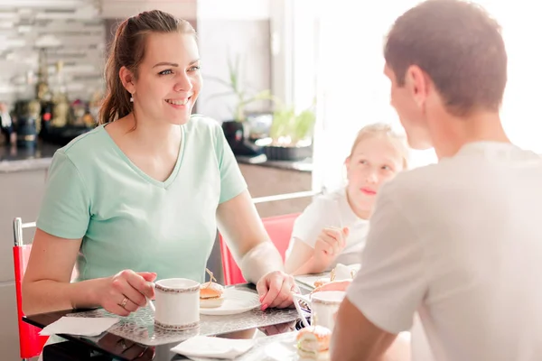 Une famille heureuse prend le petit déjeuner à une table dans la cuisine de leur appartement. La cuisine est très lumineuse et ensoleillée . — Photo