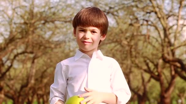 身穿白衬衫的小男孩看着摄像机 微笑着 手里拿着一个苹果 — 图库视频影像