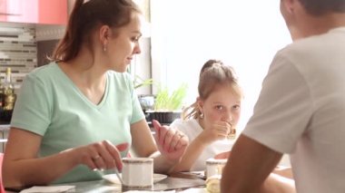 Mutlu bir aile evlerinin mutfağındaki masada kahvaltı yapar. Mutfak çok aydınlık ve güneşli. Video