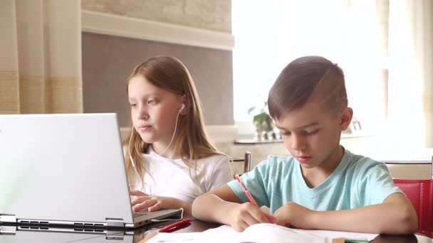 男の子と女の子 弟と妹は家で勉強します テーブルの上にはノートパソコン ノートパソコン ペンがあります 妹は兄が宿題をするのを手伝う ビデオ — ストック動画