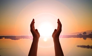 İki el gökyüzünde, ortasında güneş var.