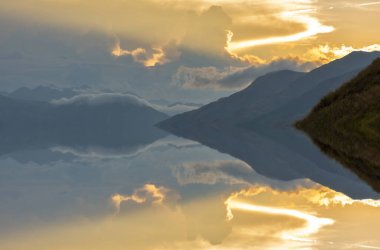 Arka planda dağlar olan bir gölde gün batımı