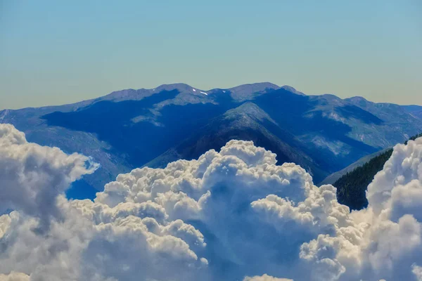 Niedrige Wolken nähern sich einem großen Berg an einem blauen Tag — Stockfoto