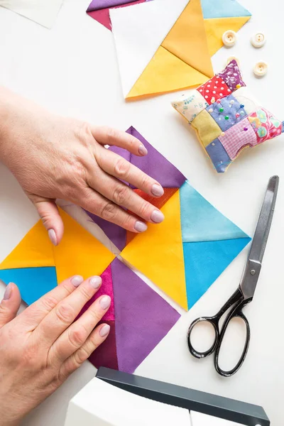 Las manos femeninas coordinan piezas geométricas de tela de color para la colcha de patchwork sobre un fondo blanco. el proceso de creación de mantas raspadas. Vista superior. plano laico . —  Fotos de Stock