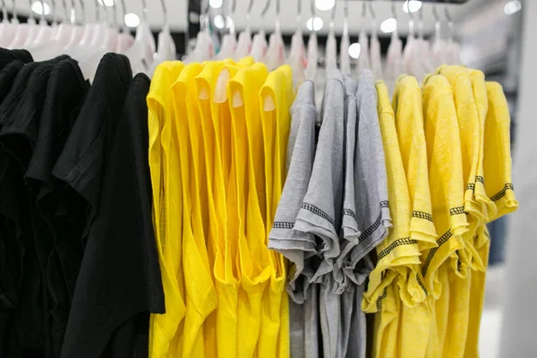 Camisetas en perchas en la tienda. Ropa en tonos amarillos. Camisetas grises. Ropa en tonos negros . — Foto de Stock