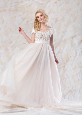 bir muhteşem gülümseyen sarışın gelin bir beyaz dantelli gelinlik hafif bir arka plan üzerinde güzel kıvırcık saçlı. gelin saç ve makyaj güzel genç model beyaz elbise döngü kadar atar.