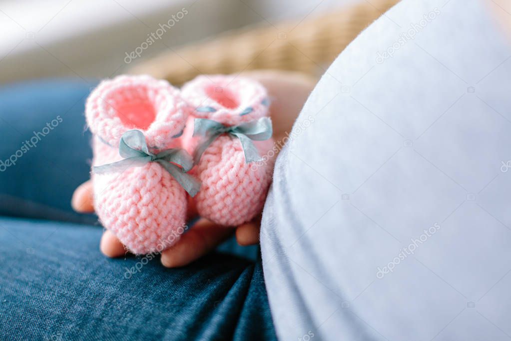 future mother knows a sex of her baby. pregnancy concept. Pregnant woman holding pink knitted baby bootees at a stomach with selective focus.