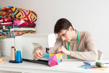Beyaz bir arka planda, el yapımı dikiş makinesi üzerinde renkli patchwork yorgan dikiş gözlük yakışıklı genç erkek terzi. bölük pörçük battaniye üretimi.