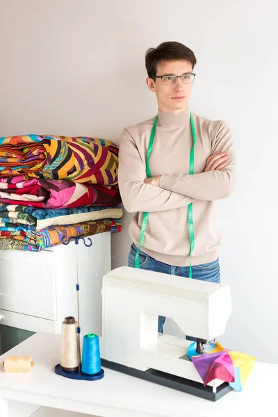 Schöner junger männlicher Schneider mit einem Stapel gefalteter farbiger Patchworkdecken auf weißem Hintergrund. viele bunte Decken im Stil Patchwork in den Händen des lächelnden Mannes, handgefertigt. — Stockfoto