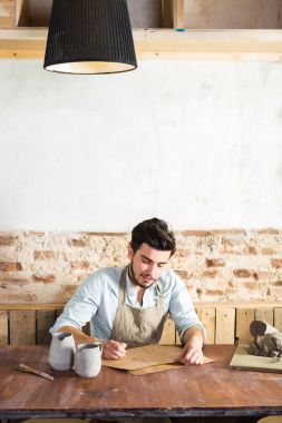 gülümseyen yakışıklı genç Meksikalı potter seramik kağıt üzerinde çizimler yapar. küçük işletme, el işi çalışmaları kavramı. Dikey metin için boş yer resimle.