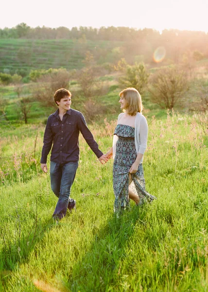 Hombres y mujeres felices caminando sobre una hierba verde en el parque en el soleado día de verano. Belleza escena de la naturaleza con estilo de vida familiar al aire libre. Feliz pareja descansando juntos en el prado, divirtiéndose al aire libre . —  Fotos de Stock