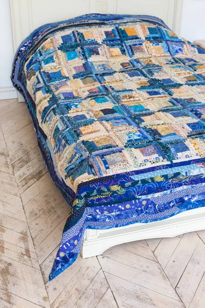 large bright double bed with a colored patchwork quilt in the white interior. blue scrappy blanket on the bed closeup.