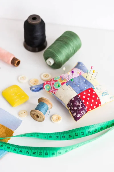 Set concept for sewing. production of patchwork quilt. measure tape, color bobbin of thread, pin cushion with sewing pins, buttons and fabric pieces on a white background. tool kit of the tailor. — Stock Photo, Image