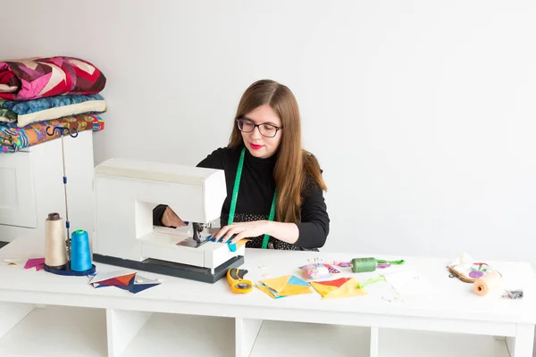 De prachtige lachende jong meisje met bril op de naaimachine. het proces van het creëren van de lappendeken. de jonge vrouw modeontwerper in een werkplaats. concept van kleine bedrijven. — Stockfoto