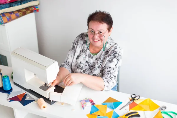 De lachende vrouw met brillen werken op de naaimachine in atelier. het proces van het creëren van de lappendeken. de vrouw modeontwerper in een werkplaats. concept van kleine bedrijven. — Stockfoto