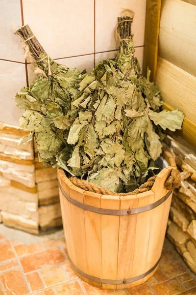 Bath accessories in traditional Russian sauna. Bath brooms from oak in wooden sauna bucket in the russian bath close up. — Stock Image Bath accessories in traditional Russian sauna. Bath brooms from oak in wooden sauna bucket in the russian bath close up. Royalty Free Stock Images