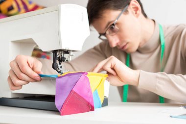 genç erkek terzi tablo parçalardan renkli kumaş dikiş makinesi ve dikiş tasarımcı patchwork çalışır.