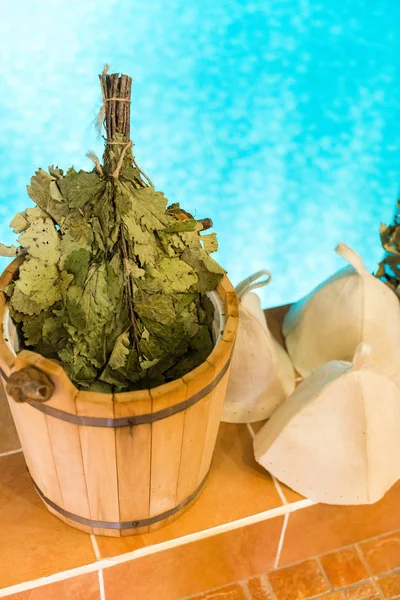 Foglia di quercia Venik con erbe essiccate in secchio sauna in legno e cappello sauna su uno sfondo piscina. Medico sauna scopa e salute Venik per il corpo . — Foto Stock