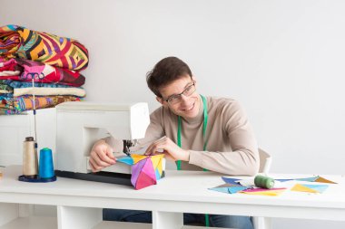 kapitone ve patchwork terzi erkek - atölye gözlük ve boyunda ölçüm bandı ile gülümseyerek terzi dikiş makinesi parlak renkli patchwork ve yan seyir ile çalışır.