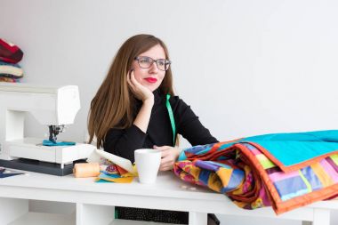 dikiş ve kapitone bir terzi - atölyesinde güzel genç bir dikiş makinesi, kumaş ve konu ile masada kollarını eğilerek kadın dinlenirken çalışma ve yan, seyir terzi