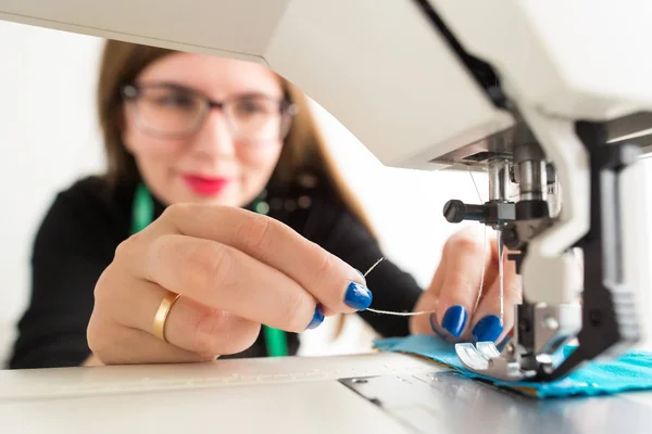 La costura y el acolchado de mano en el taller del sastre - el primer plano a las manos de la mujer hermosa con los cristales en el trabajo en la máquina de coser . — Foto de Stock