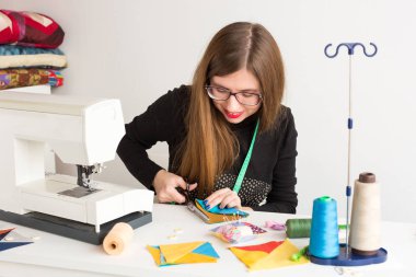 dikiş ve kapitone bir genç - bir dikiş makinesi, konu, iğne ve yastık bobinleri ile çalışma masasında makas ile dikişli kumaş kesmek kadın terzi atölyesinde