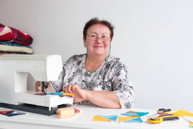 patchwork ve kapitone bir terzi kadın beyaz arka planda - atölye yaşlı kadın gözlük ile mavi ve sarı kumaş patchwork için dikiş makinesi artıkları üzerinde diker.