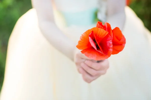 彼女に白衣を着てドレス春のポピーの圃場でポピー、農業・生産・生態、自然と夏のコンセプト - 小さな女の子の手に 2 つの赤いケシの花のクローズ アップ. — ストック写真