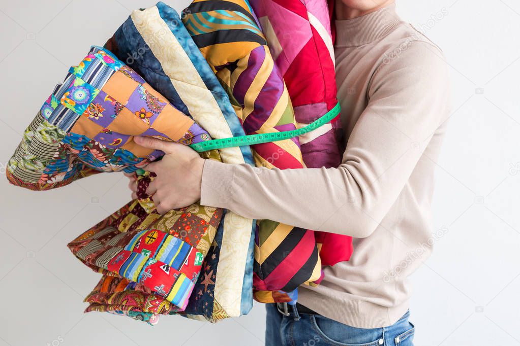 quilting and patchwork at workshop of tailor male - tailor holds in his hands near chest stitched multi-colored patchwork fabric, which are connected by the measuring tape.