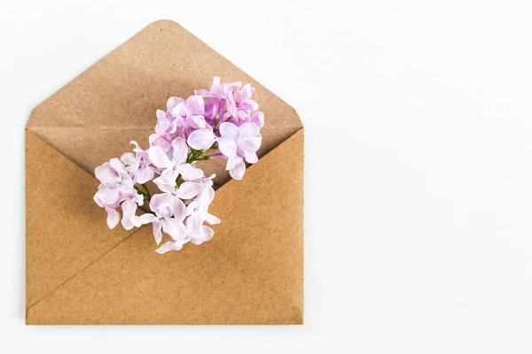 開いているクラフト紙の封筒春の花柔らかい淡い紫ライラック花いっぱい白い背景の上に敷設をクローズ アップ。平面図です。愛と提案のコンセプトです。フラットが横たわっていた。幸せなバレンタインデー. — ストック写真