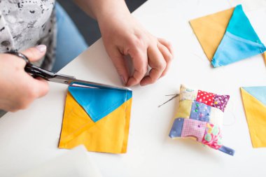 patchwork kapitone terzi kadın - atölye kapatıp terzi makas kesim kumaş patchwork üstünde okul sırası ile iplik, iğne ve yastık için mavi ve sarı artıkları iş parçacığında.