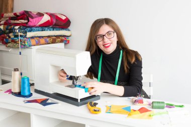 dikiş ve kapitone genç bir kadın - bir masada oturan bir dikiş makinesi ve tel, kumaşlar, iğneleri, iğne, düğmeler, güzel terzi kadın atölyesinde uzak bir tarafına bakıyor.