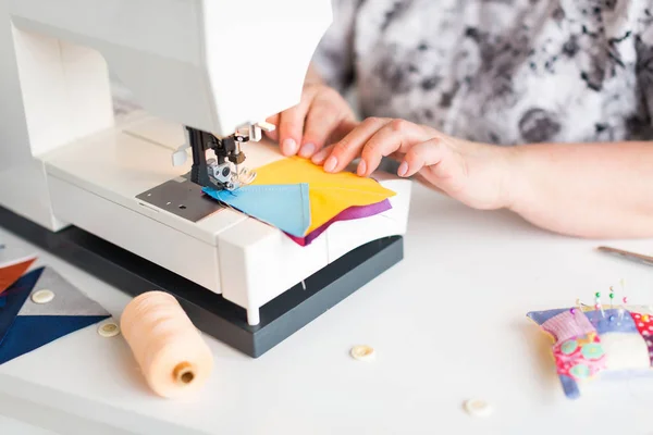 Patchwork en quilten in de werkplaats van een kleermaker vrouw op witte achtergrond - close-up op kleermaker handen en naaimachine met restjes van blauwe en gele stof voor patchworking — Stockfoto