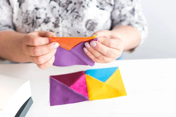 Costura y acolchado en el taller de una mujer sastre sobre fondo blanco - de cerca en las manos de una mujer sastre recoger el dibujo de telas de colores para patchwork —  Fotos de Stock