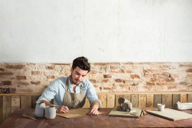 gülümseyen yakışıklı genç Meksikalı potter seramik kağıt üzerinde çizimler yapar. küçük işletme, el işi çalışmaları kavramı. Resim metni için boş alan ile.