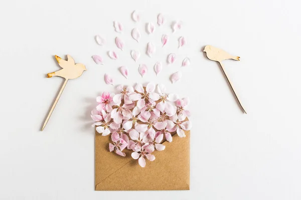 Close-up van geopende ambachtelijke papieren enveloppe vol met lente bloesem sacura bloemen op witte achtergrond. Bovenaanzicht. concept van liefde. Vlakke plaat. — Stockfoto