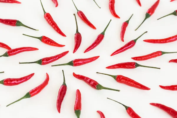 red hot chili peppers, popular spices concept - close up on decorative pattern of red hot chili with green tails on white background, beautiful collage of freely lying peppers, top view, flat lay.