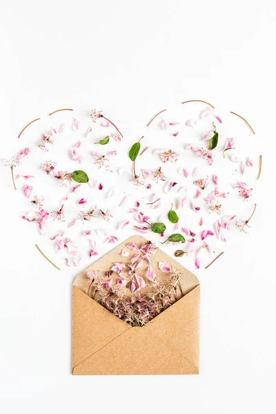 白い背景にハート型の封筒から注がれた春の花の終わり。最上階だ。愛と提案の概念です。平置きだ。ハッピーバレンタインデー。女性の日だ。3月8日。母の日. — ストック写真