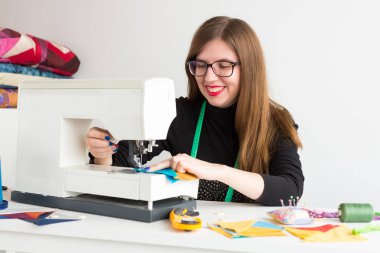 dikiş ve kapitone genç bir kadın - atölye kadar yakın bir dikiş makinesi ve konu, kumaşlar, iğneleri, iğne, düğmeleri ile terzi kadın çalışıyor.