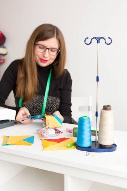 iğne işi ve genç bir kadın, bir terzi atölyesinde kapitone - gülümseyerek terzi konu, kumaşlar, iğne ile masada renkli bez parçaları ile iş yerinde bardaklarda