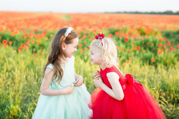 女の子のモデル、ポピー、幼年期、ファッション、自然と夏のコンセプト - 2 人の若いガール フレンド笑う赤 poppiesin の開花フィールド上彼らはエレガントな青と赤の晴れ着を着ています。. — ストック写真
