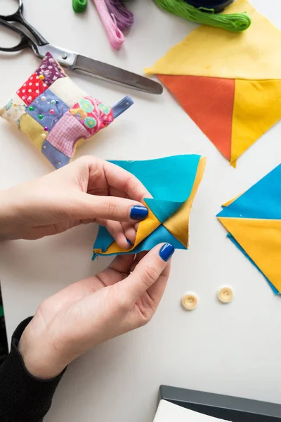 Naaien en quilten in de werkplaats van een kleermaker op witte achtergrond - close-up op de handen van een kleermaker holding kladjes van weefsels liggend op een witte tafel met knoppen, pin kussen, schaar. — Stockfoto