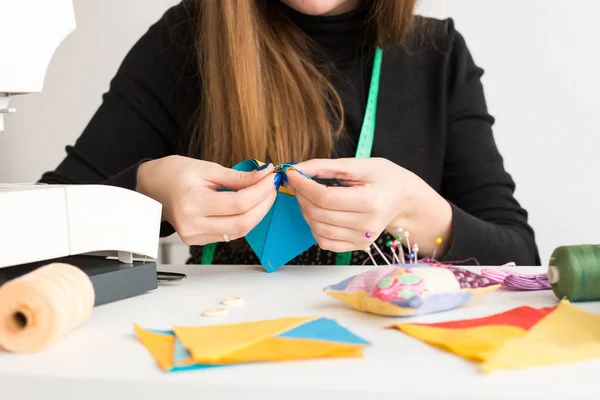 Naaien en quilten in de werkplaats van een jonge vrouw, een kleermaker op witte achtergrond - close-up van handen van een vrouw kleermaker steken een naald en stukken van kleurrijke stoffen — Stockfoto