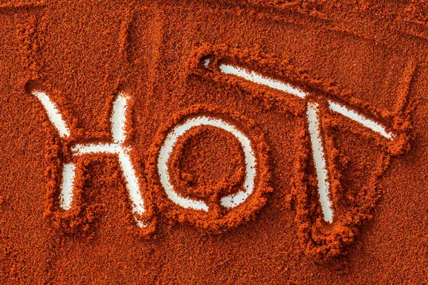 chili red hot pepper, concept of popular spice - on background pattern of dry ground spices written word HOT by the finger of a man, word HOT on background of brown pepper powder, flat lay, top view.