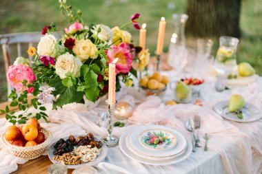 piknik, yaz, tatil kavramı - güzel masa yeşil çim ağaç, Ajur beyaz masa örtüsü, renkli yaz buket Şakayık ve gül, meyve, şamdanlar, Züccaciye, limonata, ayarlama.
