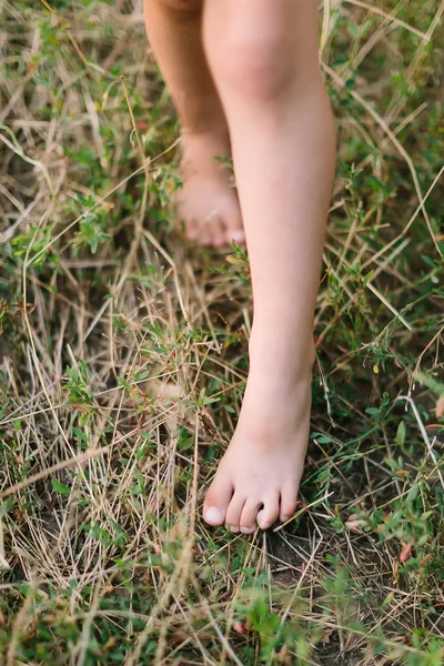 childhood, nature, ecology and plant concept - close-up of bare feet of young girl marching on summer green grass, between grass is a dark soil, black soil, selective focus.