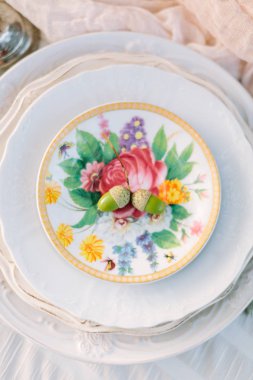 piknik, gıda, tatil kavramı - dikey beyaz ve açık tonları, ile üst plaka üzerinde iki meşe palamutları meşe delikanlı güzel renkli çiçeklerle dekore edilmiş çeşitli tatil temiz tabak yığını.