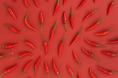 red hot chili peppers, popular spices concept - close up on decorative pattern of red hot chili with green tails on red background, beautiful collage of freely lying peppers, top view, flat lay. clipart